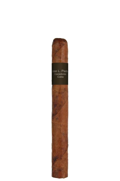 A close-up of a Jose L. Piedra Cazadores cigar, showcasing its rustic brown wrapper and classic band design. The cigar rests on a wooden surface, highlighting its traditional Cuban craftsmanship and bold, earthy character.