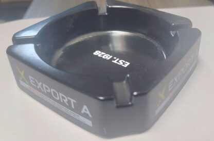 Export A Black Ashtray with sleek matte finish and embossed logo, placed on a wooden tabletop."