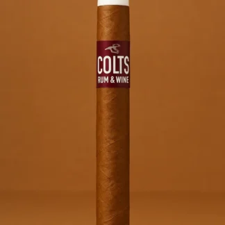 Single Colts Rum & Wine cigar with white tip, upright on a warm brown studio background.